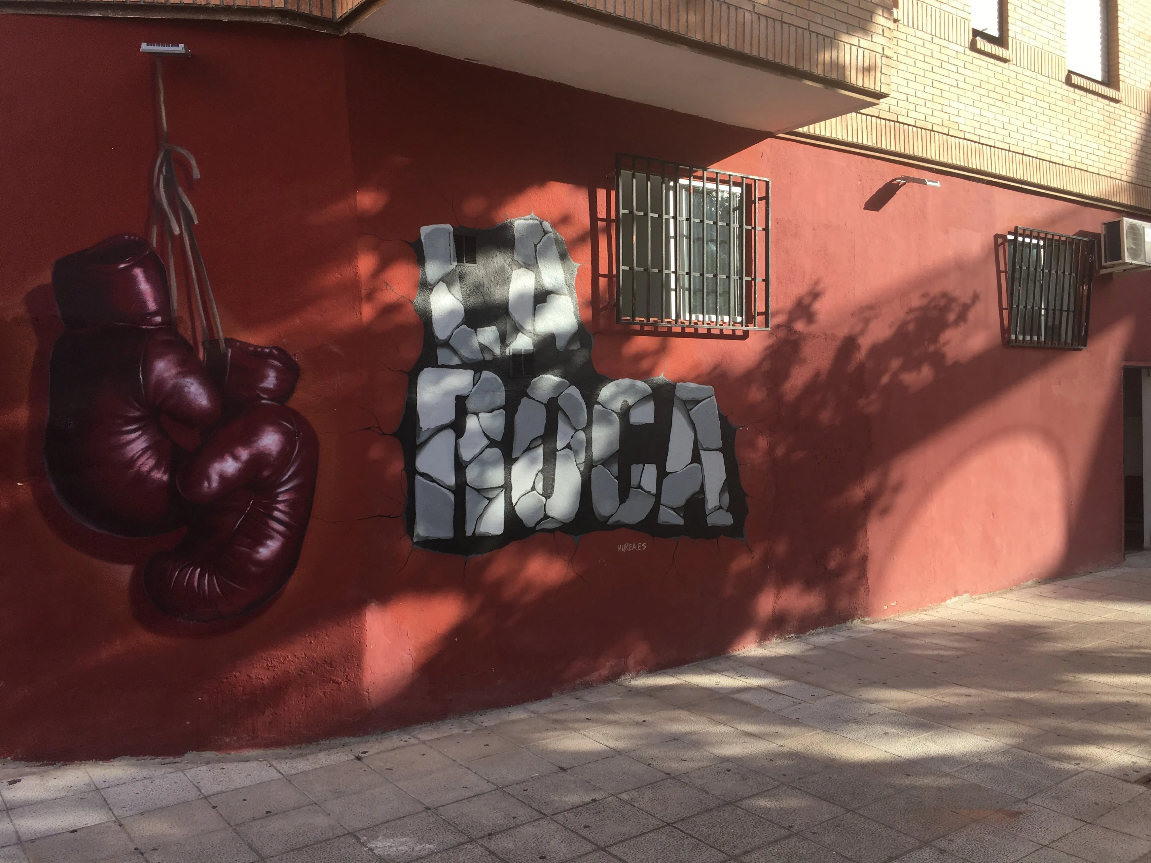 Fachada de La Roca: mural con unos guantes de boxeo y el nombre del gimnasio en piedra sobre la pared roja